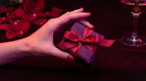 Une main délicate tenant un cadeau de mariage élégant sous un éclairage néon violet et rouge.