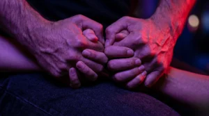 Gros plan macro sur des mains jointes avec force, soulignant l'intensité de la passion sous un éclairage rouge.