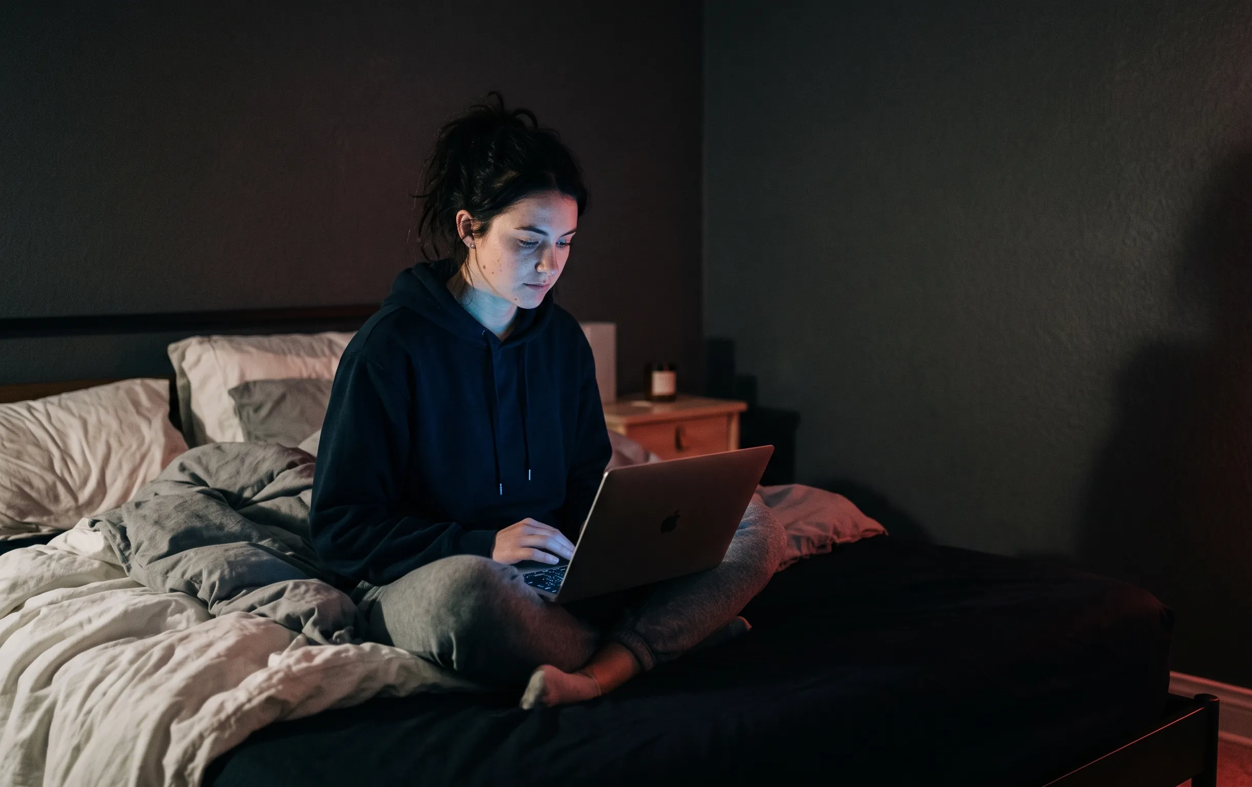 ai girl : Une personne seule face à son écran dans une chambre sombre baignée d'une lumière néon rouge cerise et bleue